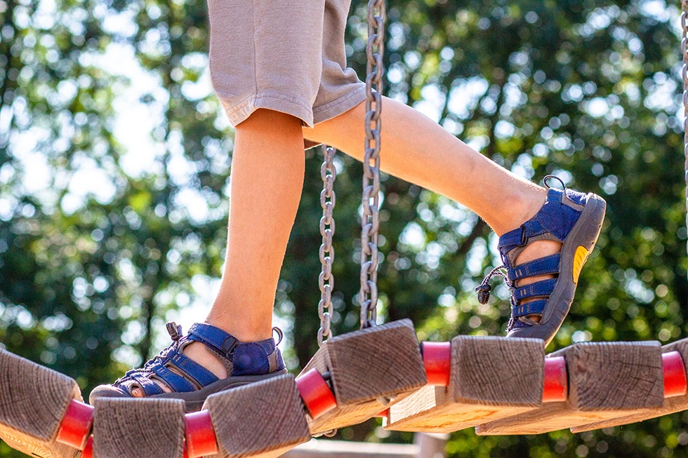 Nahaufnahme von Kinderfüßen, die über eine Hängebrücke auf den Spielplatz gehen